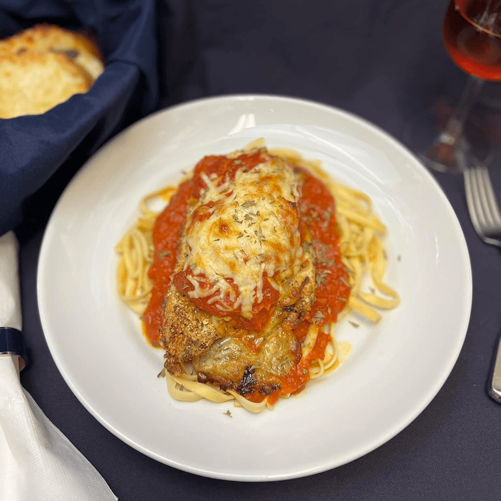 A plate of chicken parmesan topped with marinara sauce and melted cheese, served over fettuccine pasta.