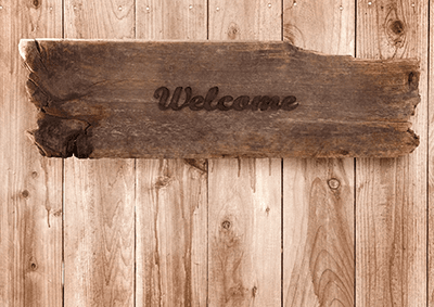 Wooden sign with the word "Welcome" carved into it, set against a rustic wood background.