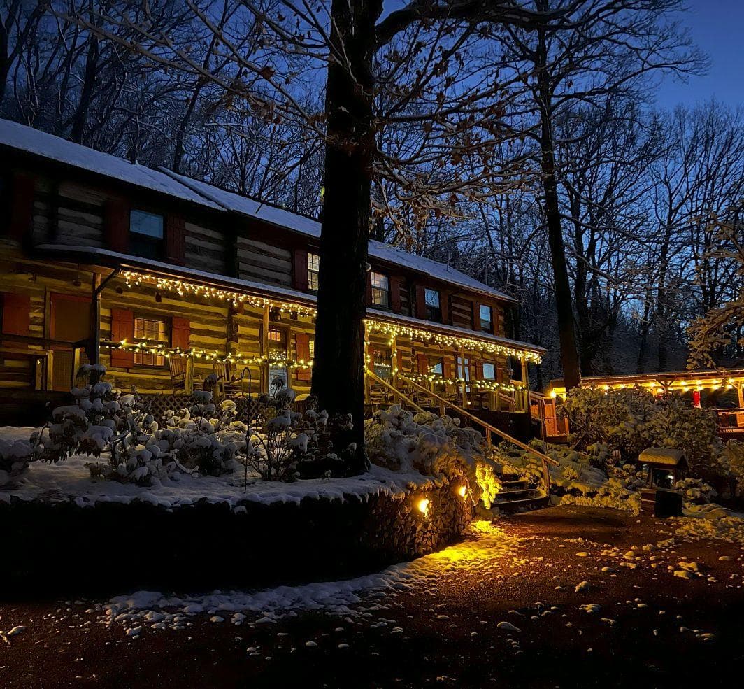 A snow-covered cabin illuminated by warm lights under a twilight sky.
