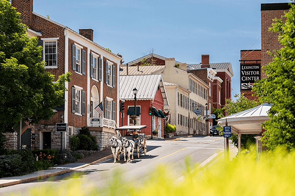 A horse-drawn carriage travels down a quaint street lined with historic buildings and a visitor center.